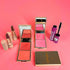 Makeup products including lipsticks, blush, and mascara on a pink background